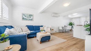 A modern living room with a blue sofa, a coffee table, and a dining area with a white table and chairs.