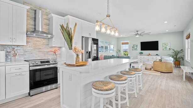 A modern kitchen with white cabinetry, a stainless steel range hood, and a large island with bar stools. - 2min Walk to Beach w Hot Tub, Centrally Located! (Oak Island)