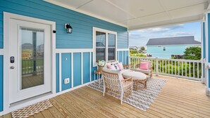 A covered porch with a blue exterior, white trim, wicker furniture, and a view of a neighboring house. - 2min Walk to Beach w Hot Tub, Centrally Located! (Oak Island)