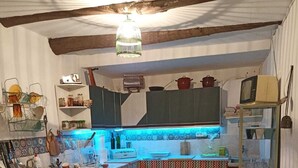 A compact kitchen with a tiled backsplash, a hanging light fixture, and a small dining area with a patterned tablecloth. - Bienvenidos a Casa Violeta (Atalbéitar)