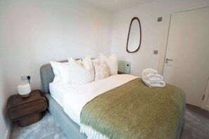Un lit bien fait, avec des oreillers, une table de chevet avec une lampe et une serviette pliée posée sur le lit.