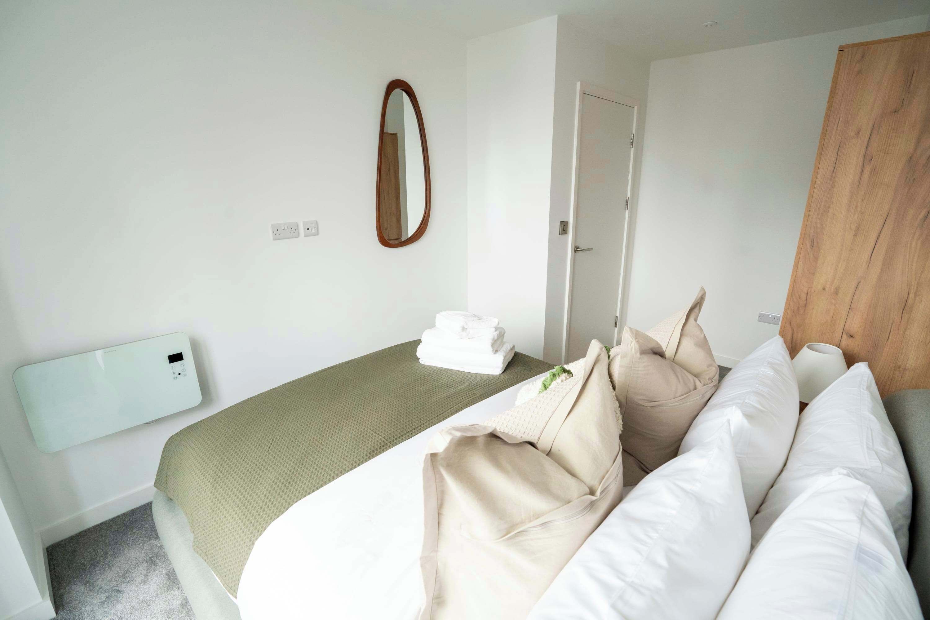 A hotel room with a bed, a bedside table, a mirror, a wooden wardrobe, and a wall-mounted air conditioning unit.