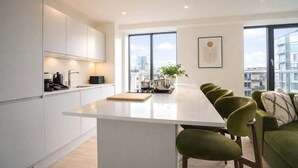 A modern kitchen with a central island, large windows, and a view of the city. - Organika Suite & 2BR Luxury w/ Skyline Views & Gym Access! (Greater Manchester)
