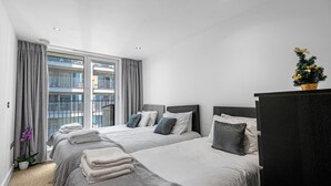 Een hotelkamer met twee bedden, grijze beddengoed, een groot raam met gordijnen, een kleine potplant en een decoratieve kerstboom.
