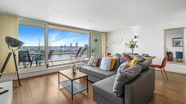 Een moderne woonkamer met een groot raam, een grijze bank, een eettafel en uitzicht op een stadsgezicht.