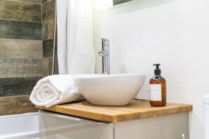 A bathroom with a white sink, a wooden countertop, a towel, and a bottle of soap.