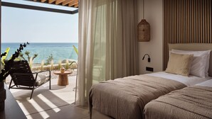 Ein modernes Hotelzimmer mit einem großen Bett, Meerblick, Holzboden und einem kleinen Tisch mit Stuhl davor.