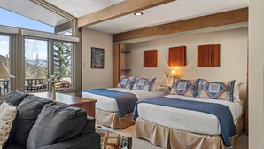 A room with two beds, a sofa, a table, and a window with a view of mountains. - Lichenhearth 17 (Snowmass Village)