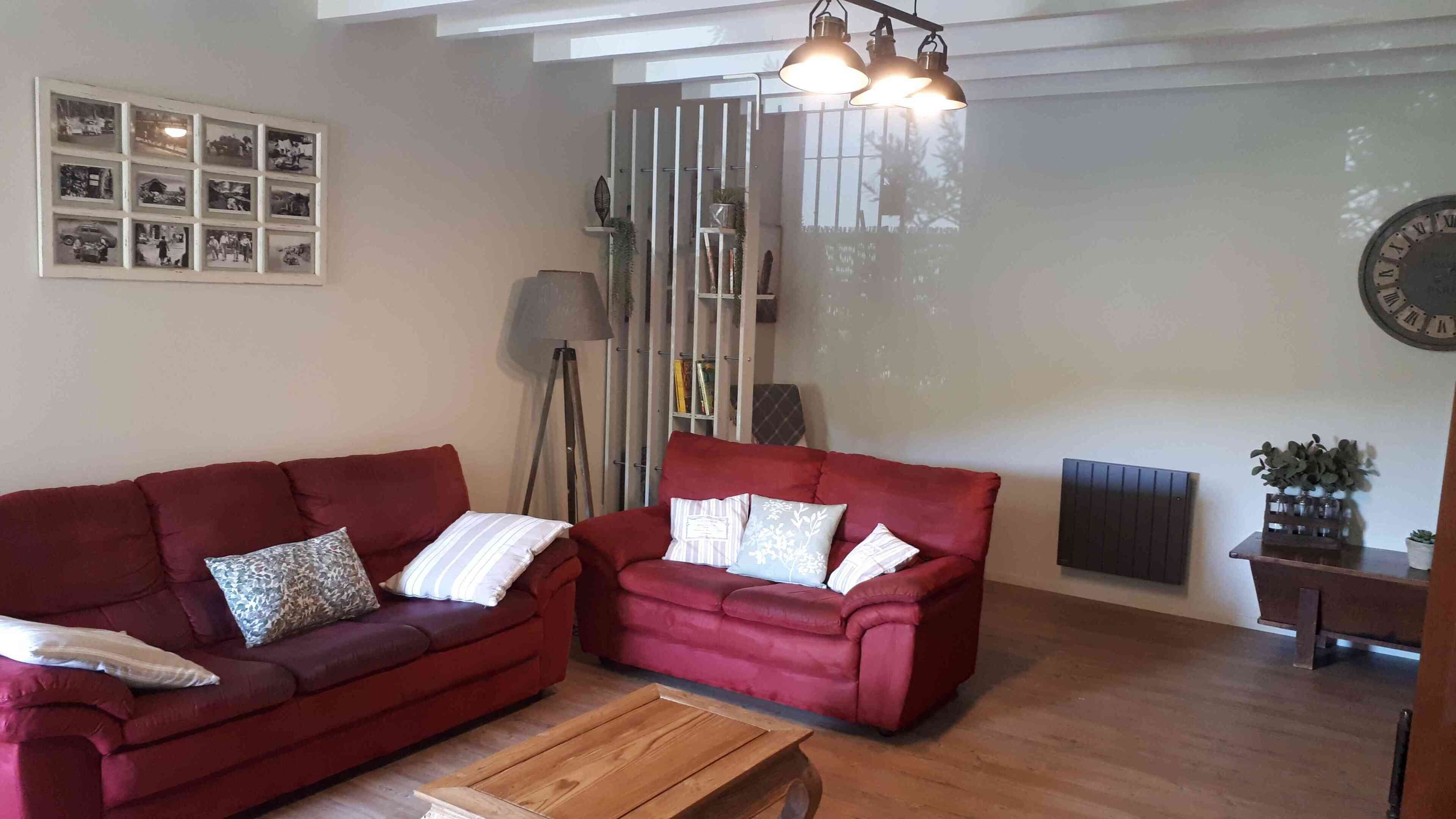A living room with two red sofas, a wooden coffee table, a clock, and a framed photo collage on the wall.