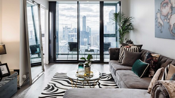 Un salon moderne avec vue sur la ville, comprenant un canapé, une table basse et un grand miroir.