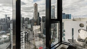 Une chambre située dans un immeuble de grande hauteur, offrant une vue sur la ville, dotée de grandes fenêtres et d’un fauteuil en osier.