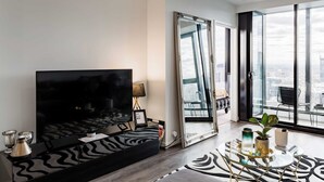 Un salon moderne doté d’un grand téléviseur à écran plat, d’un canapé, d’une table basse et offrant une vue sur la ville grâce à de grandes fenêtres.