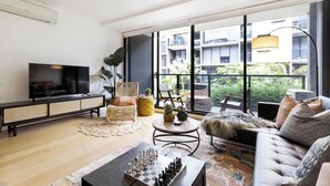 A modern living room with a flat-screen TV, a sofa, a coffee table, and a chessboard. - Tropical courtyard sanctuary near Glenferrie Rd (Hawthorn)