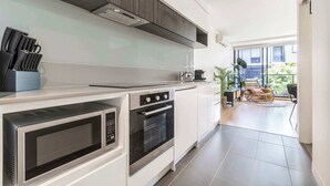 A modern kitchen with built-in appliances, a dining area with a view, and a cozy seating arrangement. - Tropical courtyard sanctuary near Glenferrie Rd (Hawthorn)