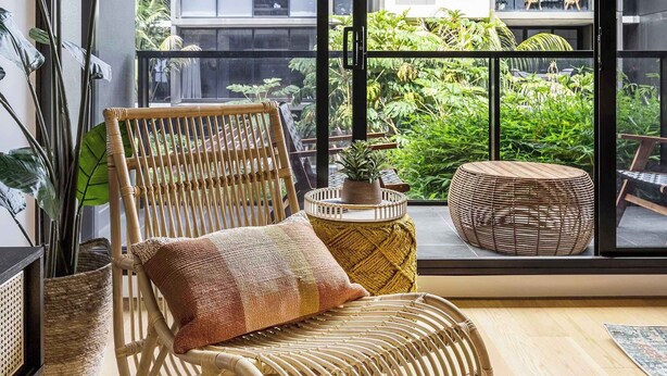 A balcony with a wicker chair, a woven rug, and a view of a building with balconies. - Tropical courtyard sanctuary near Glenferrie Rd (Hawthorn)