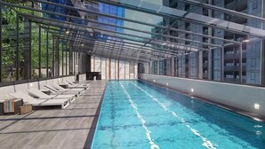 Una piscina con techo de cristal, sillas de descanso y vistas a la ciudad.