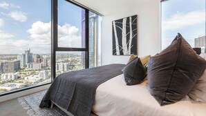 Un dormitorio con un ventanal grande, una cama con ropa de cama oscura y vistas a la ciudad.