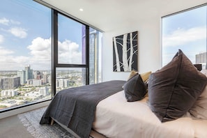 Un dormitorio con un ventanal grande, una cama con ropa de cama oscura y vistas a la ciudad.