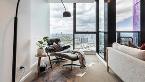 Un salón moderno con vista a la ciudad, una silla negra, un sofá, una lámpara y una mesita con una planta.