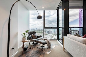 Un salón moderno con vista a la ciudad, una silla negra, un sofá, una lámpara y una mesita con una planta.