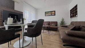 Ein modernes Wohnzimmer mit Essbereich, einer Couch, einem Couchtisch und einem Fernseher.