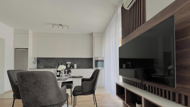 Eine moderne Küche mit weißen Schränken, einem Essbereich mit zwei Stühlen und einem großen Flachbildfernseher, der an einem Holzpaneel befestigt ist.