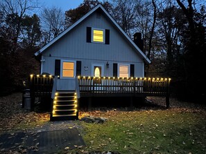 A house with a porch, a staircase, and a deck with string lights. - Beautiful & cozy chalet in the Pocono Mountains awaits! Discover all-season fun! (Tobyhanna)