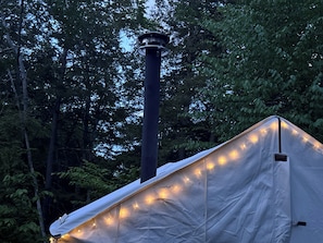 A tent with a chimney, surrounded by trees.