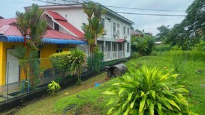 A two-story building with a red roof and a white facade, surrounded by greenery and a fence. - Hotel O D Qamar Motel (Langkawi)