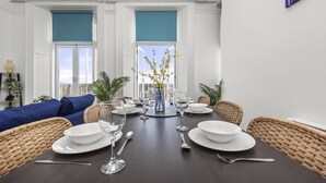 A dining area with a dark wooden table set for four, surrounded by wicker chairs, with a view of the sky through a window with a blue blind. - The Cheeky Chappie By My Getaways (Brighton)