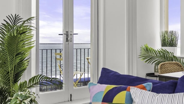 A room with a large window, a sofa with colorful cushions, and a potted plant. - The Cheeky Chappie By My Getaways (Brighton)