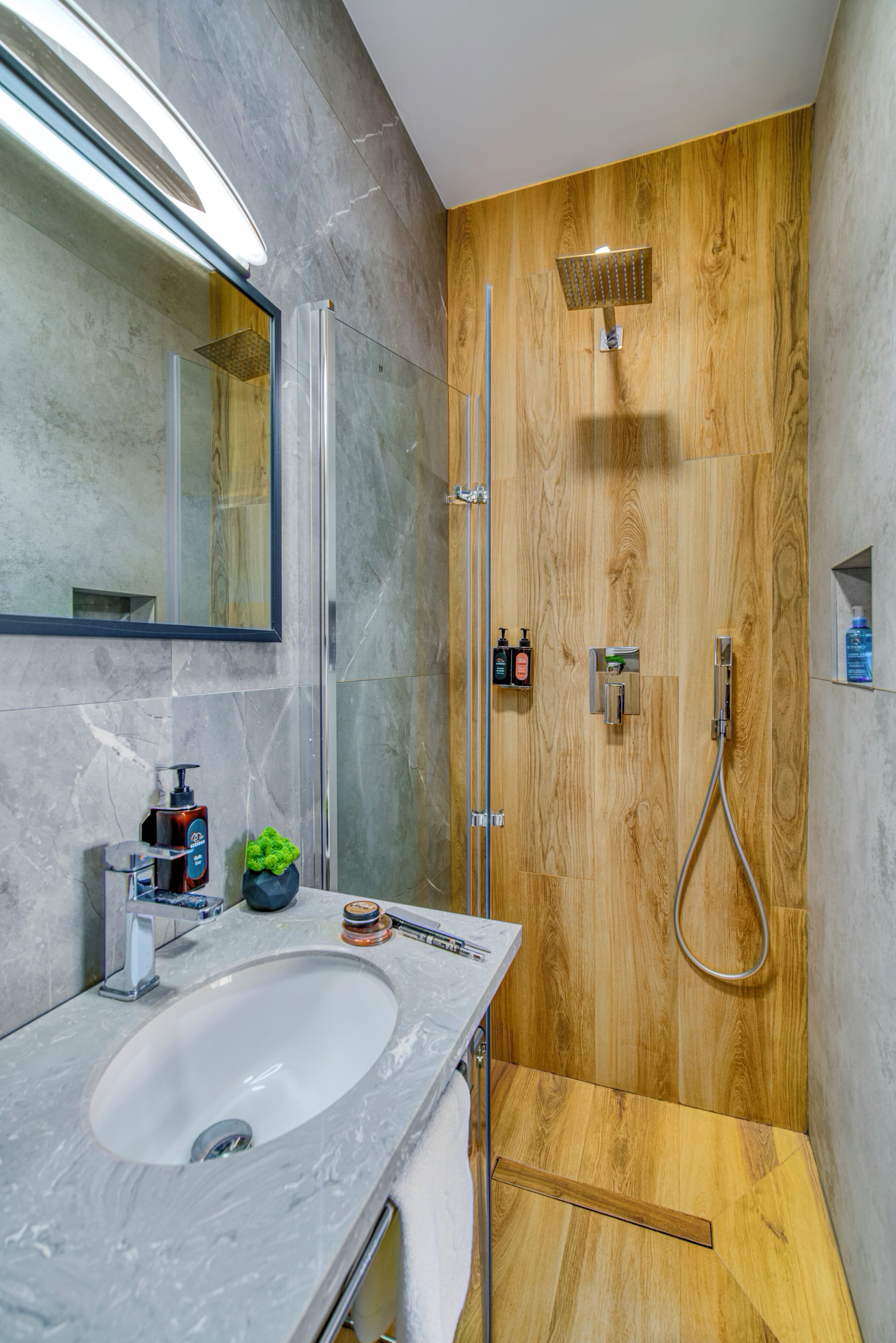 Une salle de bain moderne avec un lavabo en marbre, une cabine de douche en bois et un miroir doté d’un éclairage intégré.