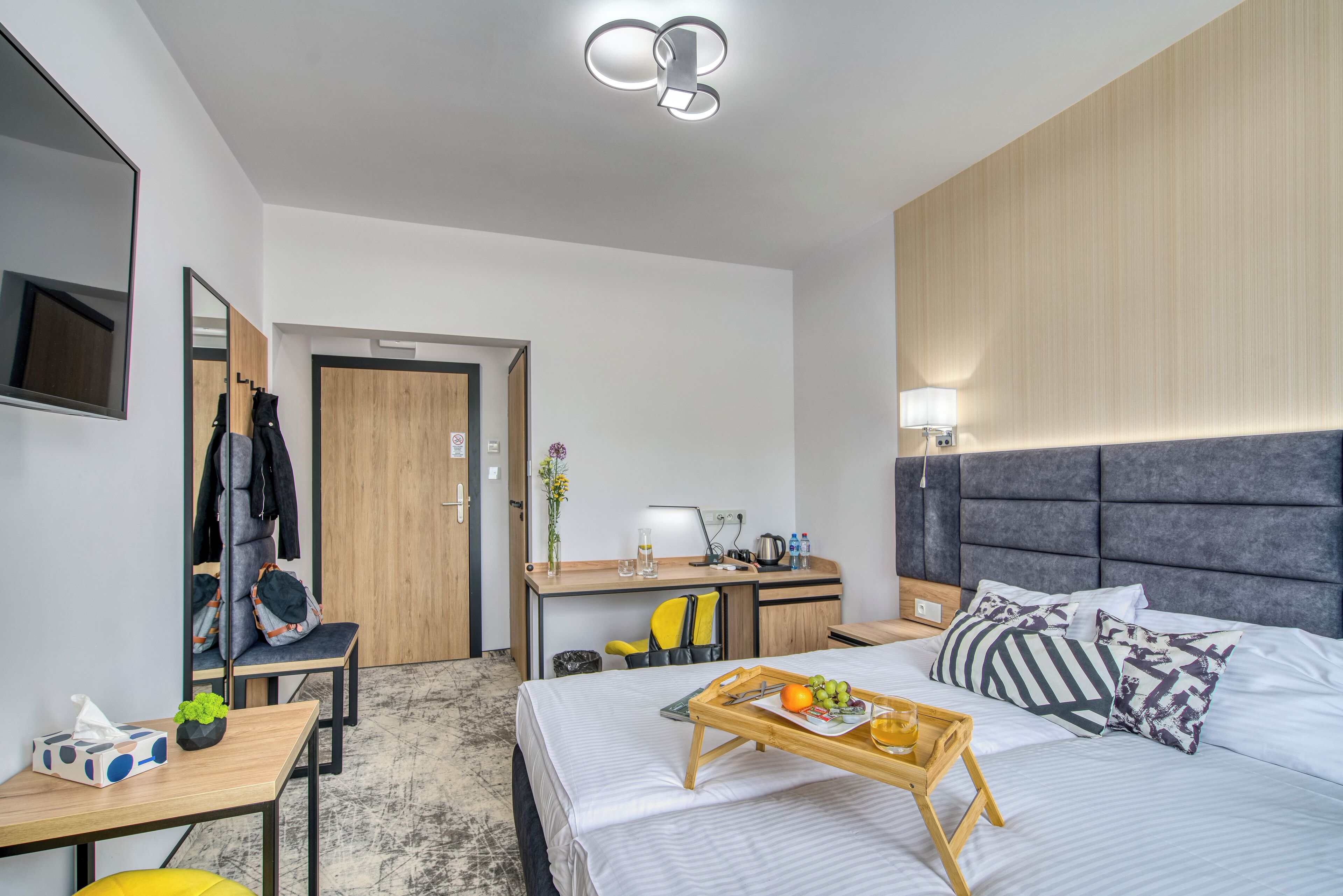 A modern hotel room with a bed, bedside table, desk, and a mirror.
