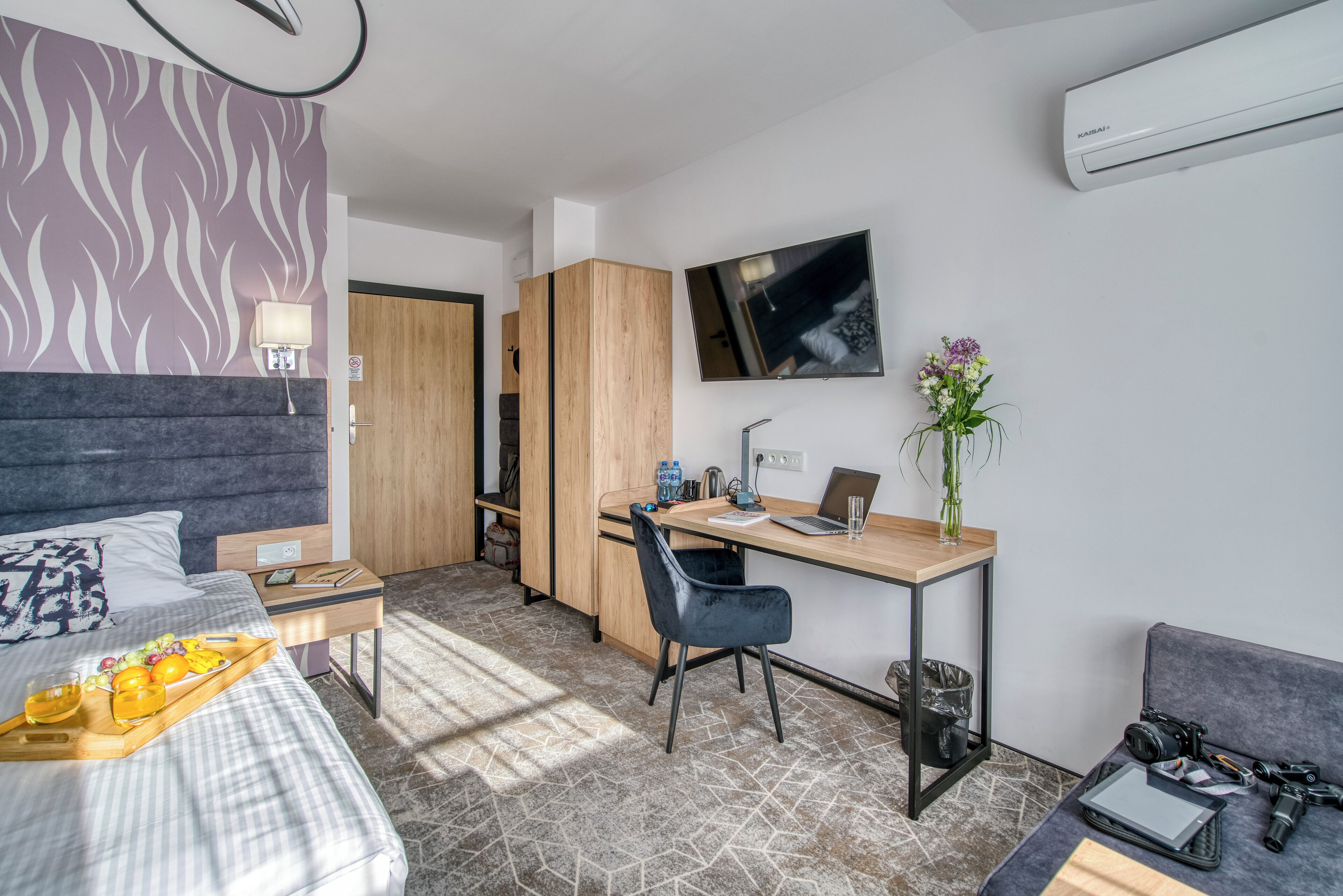 A modern hotel room with a bed, desk, chair, and a small sitting area.