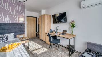 A modern hotel room with a bed, desk, chair, and a small sitting area.