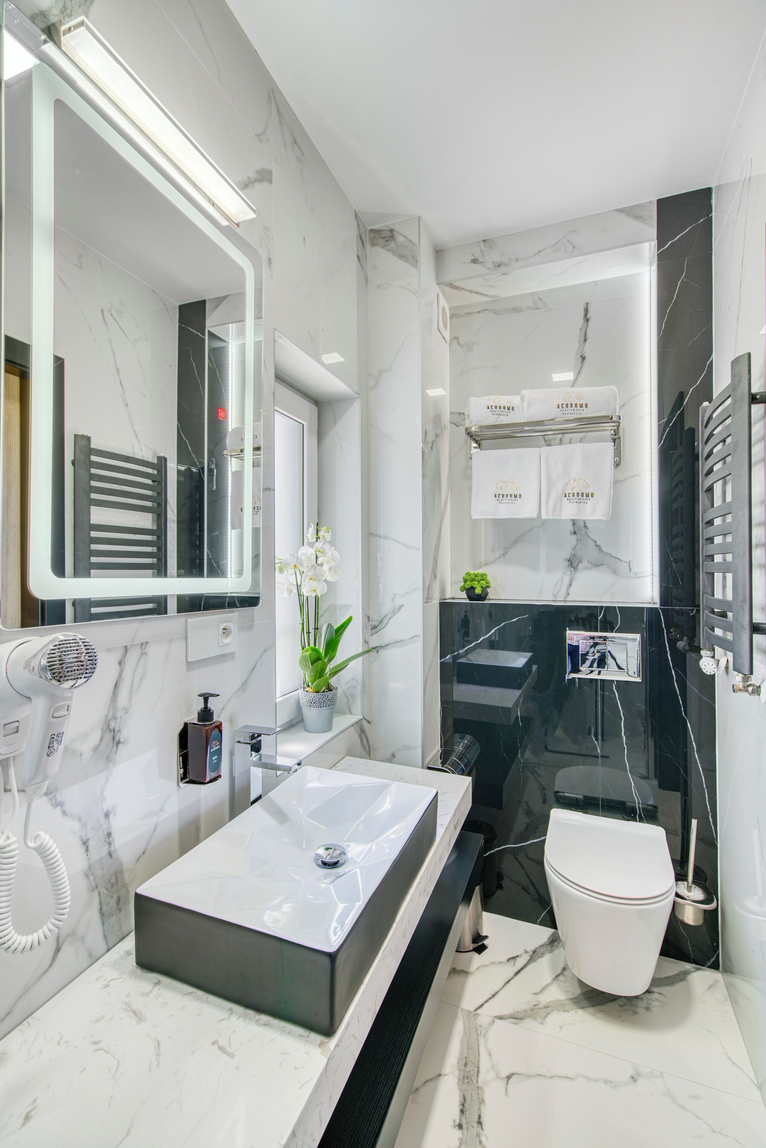 A modern bathroom with a marble sink, a large mirror, a towel rack, and a toilet.
