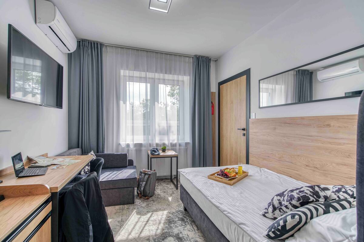 A hotel room with a bed, desk, chair, and a small table with a tray of fruit.