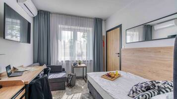 A hotel room with a bed, desk, chair, and a small table with a tray of fruit.