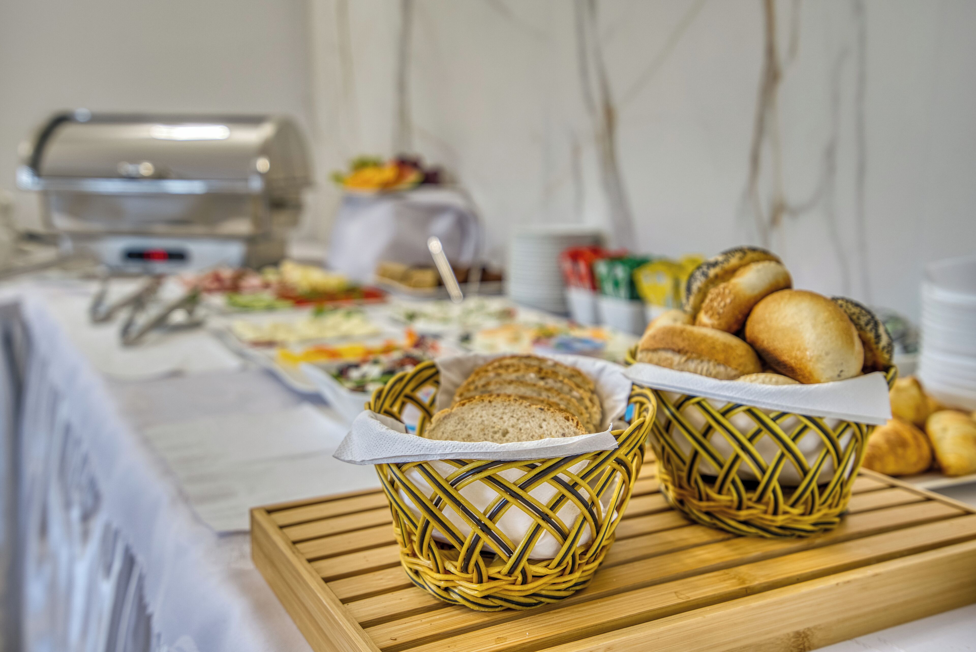 A buffet table with various food items and baskets of bread.