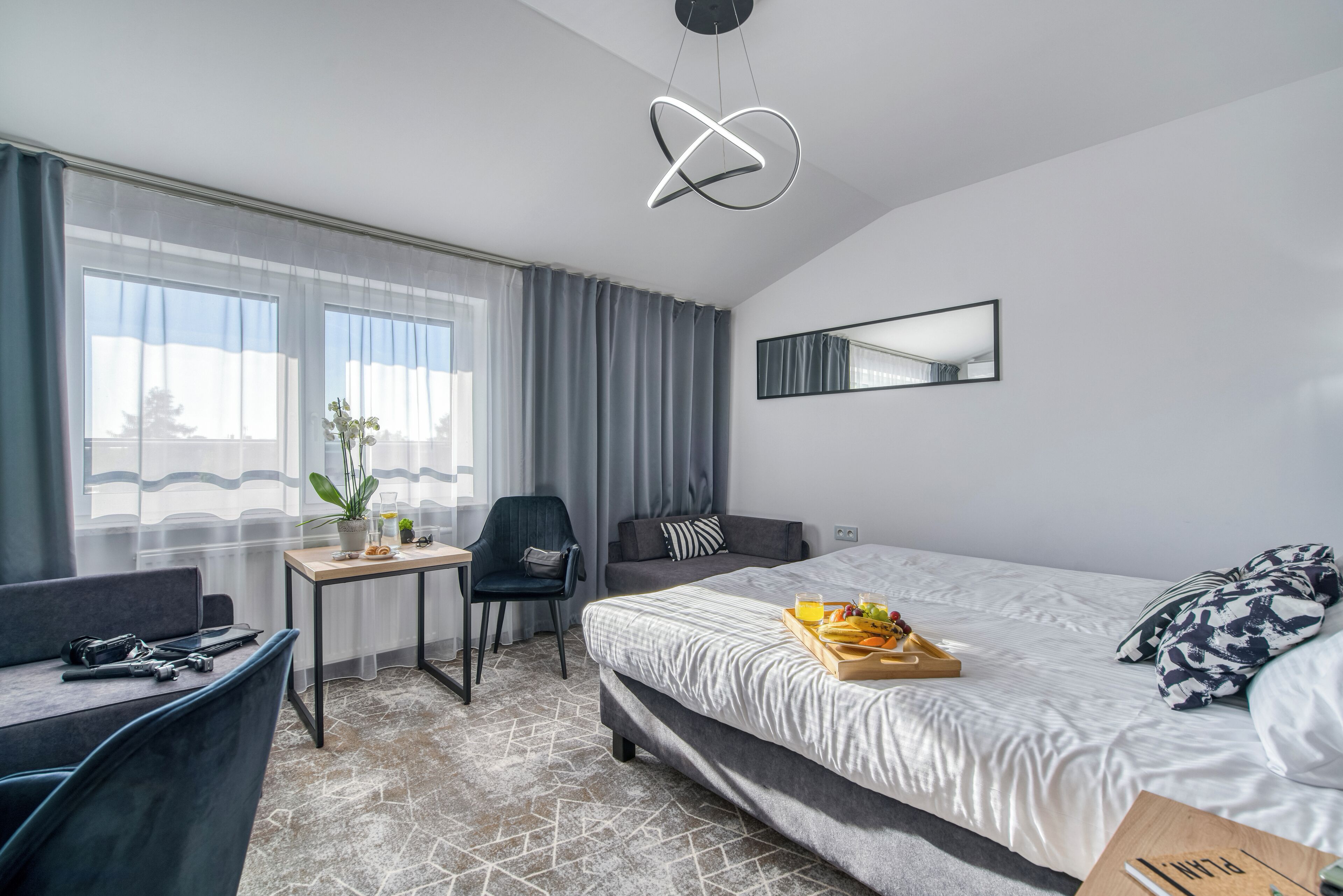 A modern hotel room with a bed, a desk, a chair, and a large window.