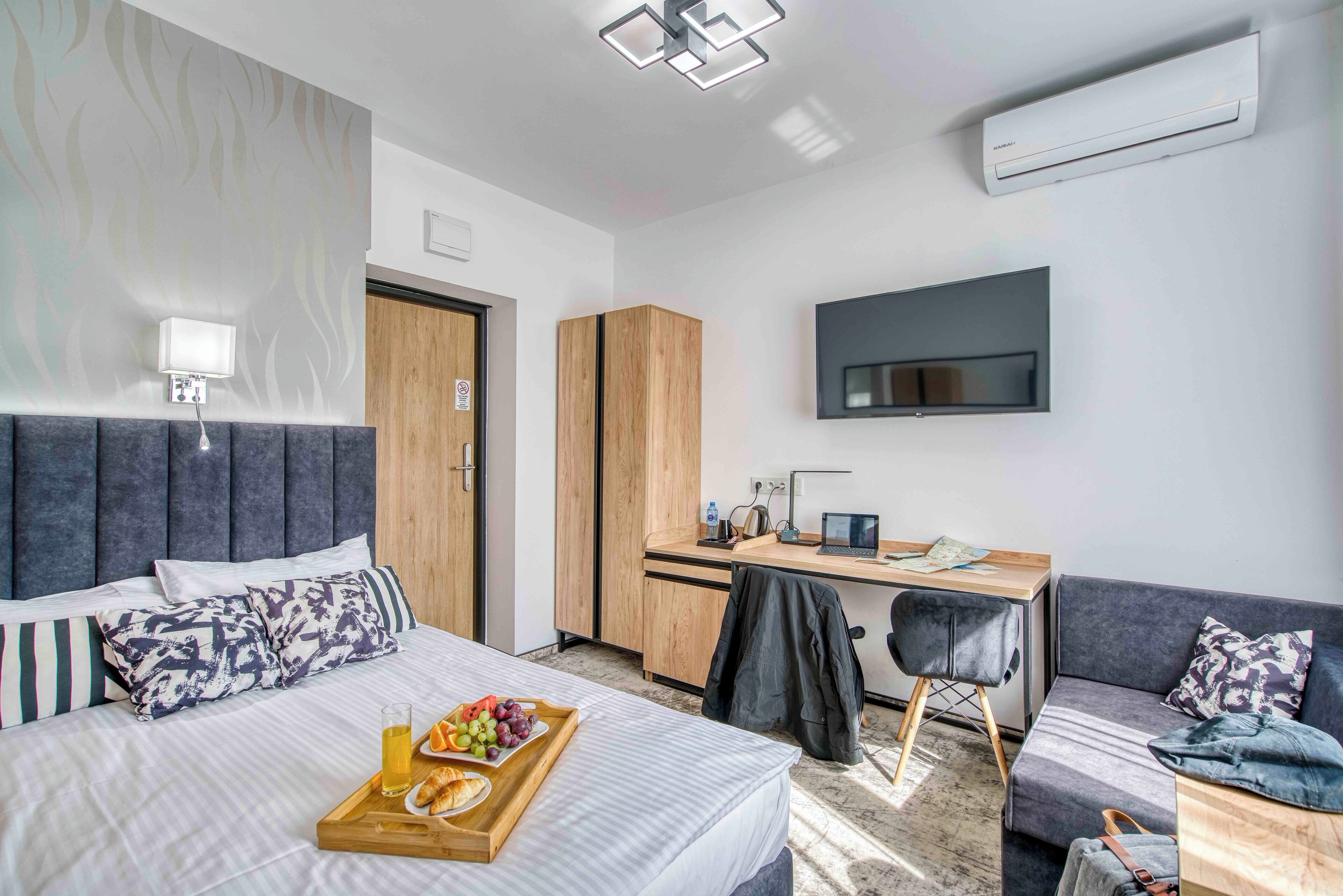 A modern hotel room with a bed, a desk, a TV, and a sofa.