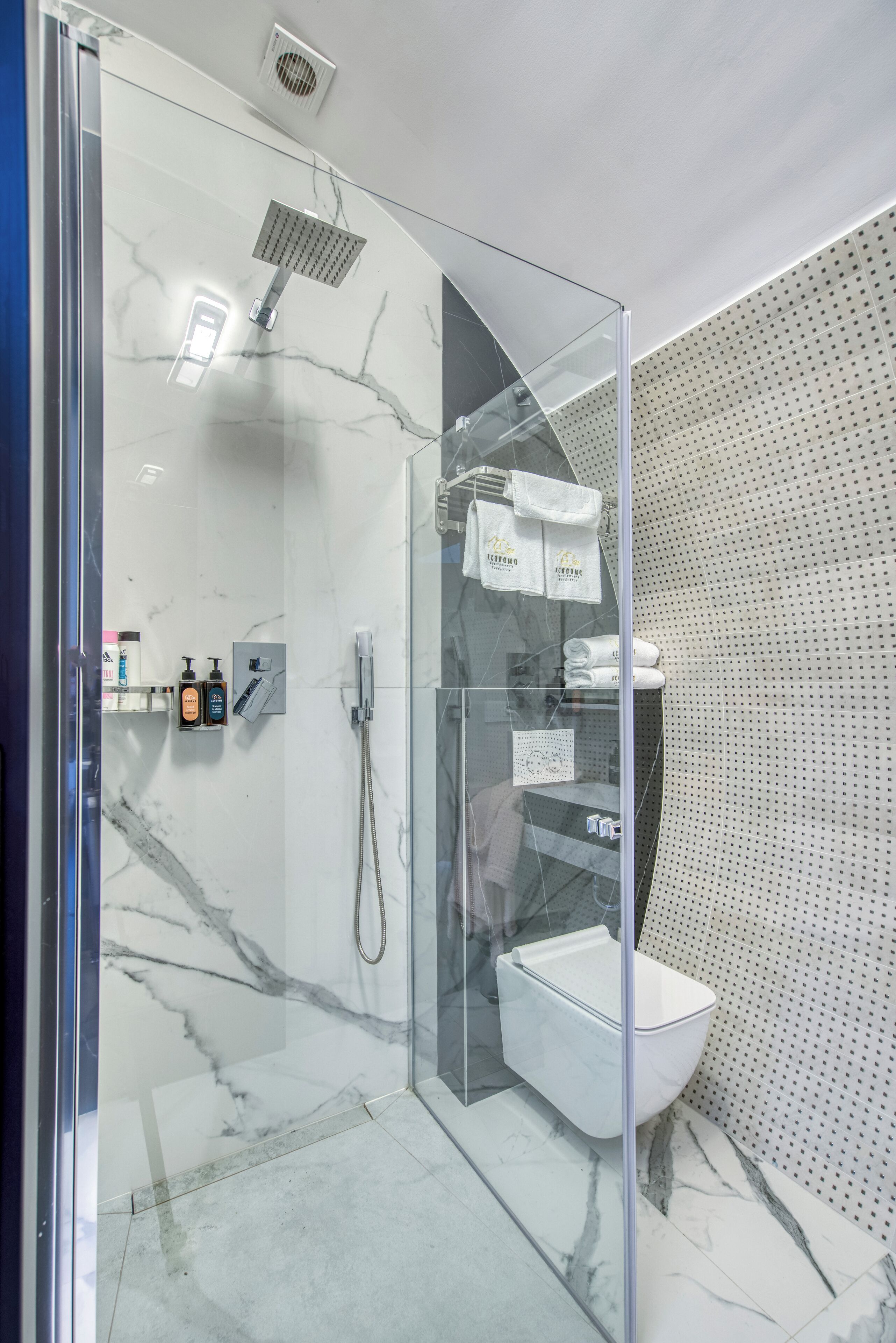 Un baño moderno con ducha de vidrio, inodoro blanco y piso de mármol.