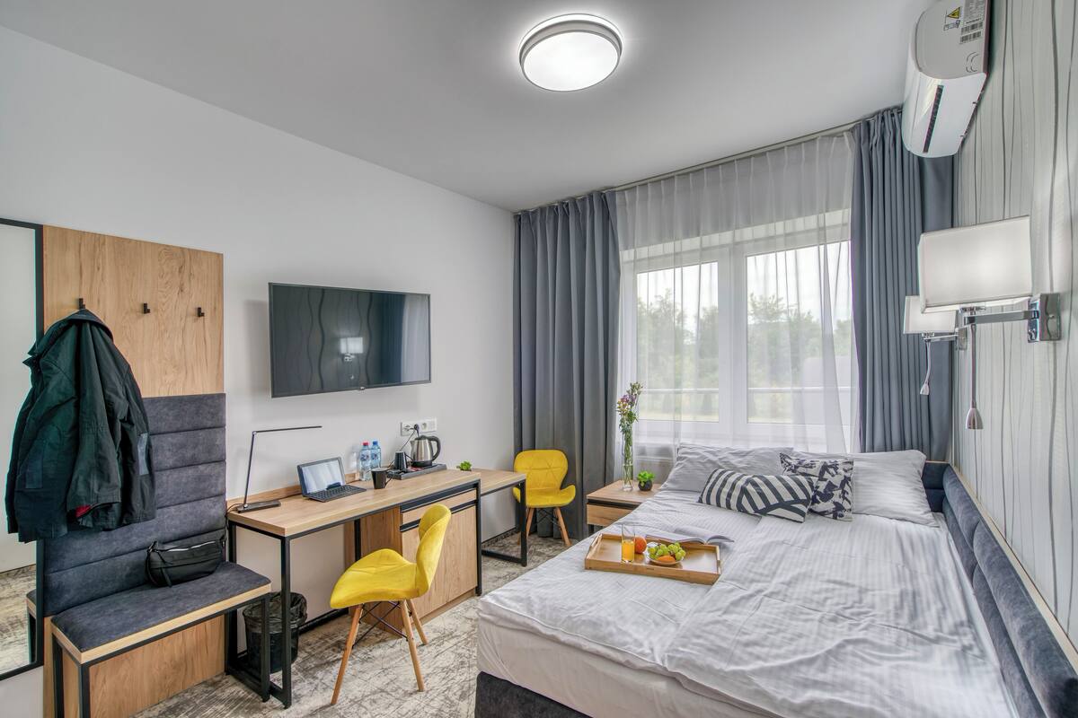 A modern hotel room with a bed, desk, chair, TV, and a window with curtains.