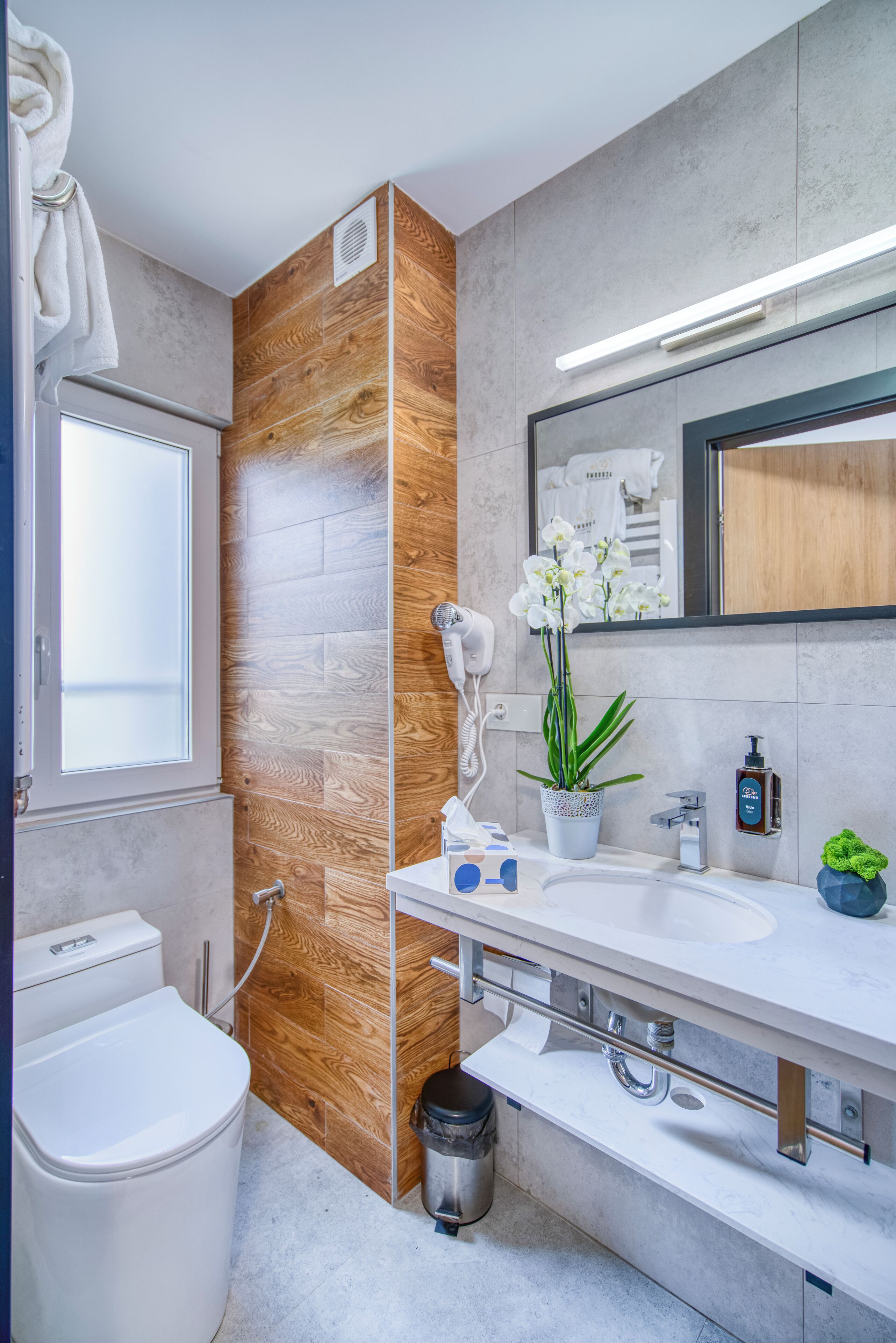 A modern bathroom with a wooden accent wall, a white sink, a mirror, and a toilet.