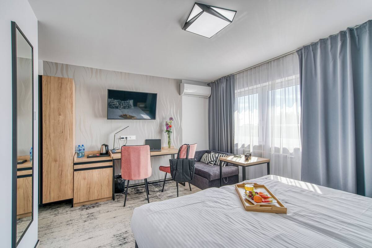A hotel room with a bed, a desk with a computer, a chair, a sofa, and a TV.