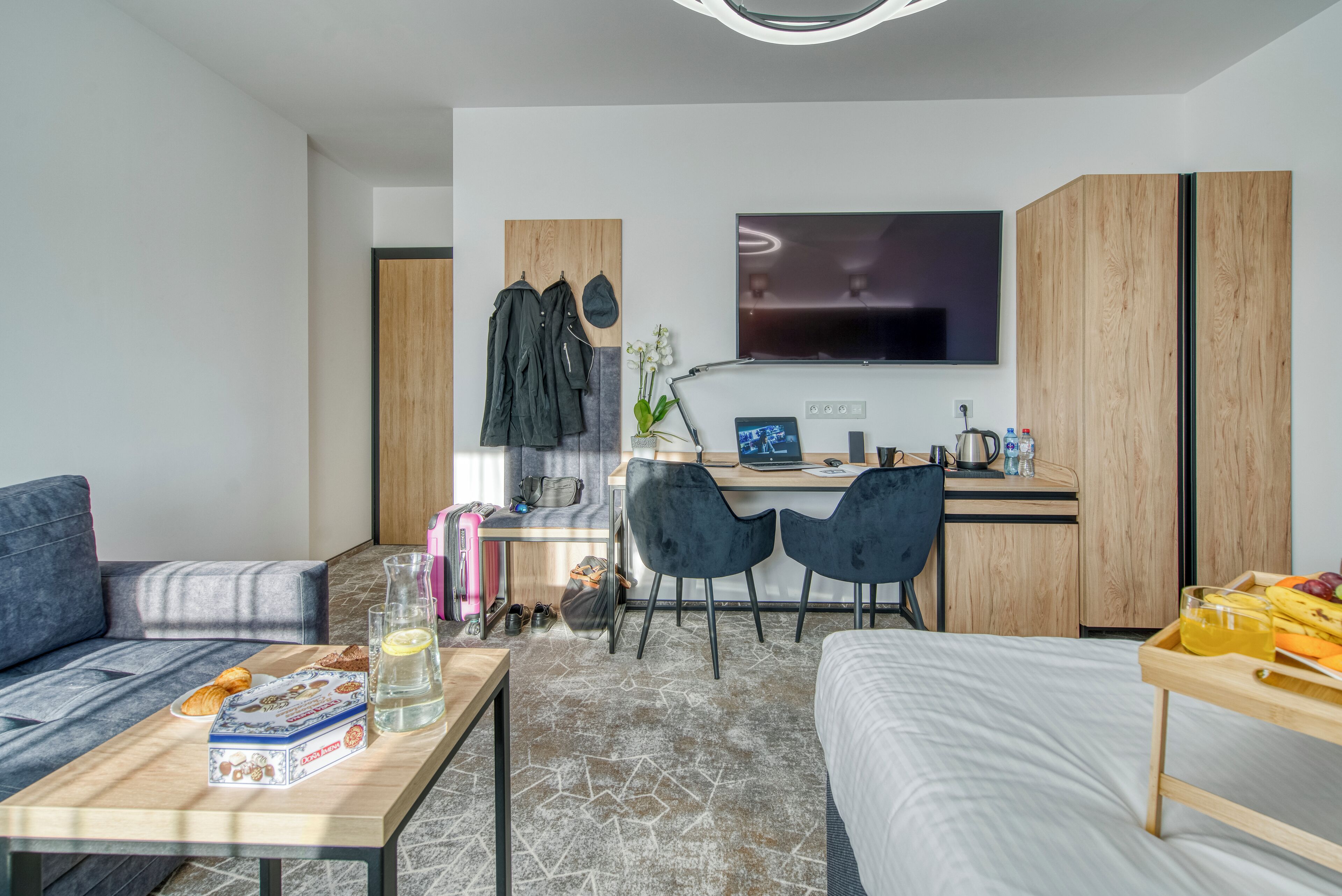 Een moderne hotelkamer met een bed, een bank, een bureau met een laptop, een televisie en een kitchenette.