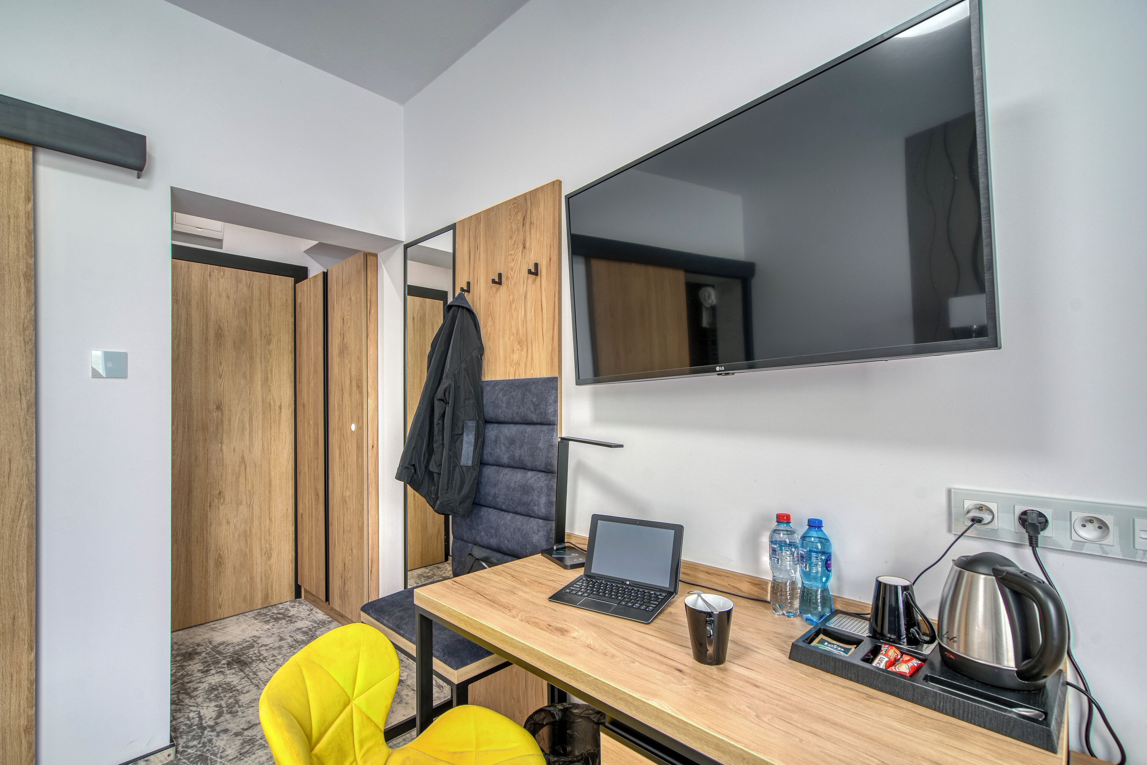 Een kleine kamer met een houten bureau, een laptop, een stoel, een spiegel en een kapstok.