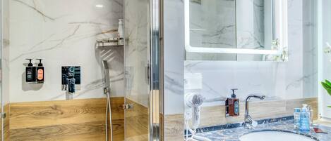 Un baño moderno con ducha envuelta en vidrio, pared revestida de mármol, pared decorativa de madera, lavamanos con encimera de mármol y espejo sobre el lavamanos.