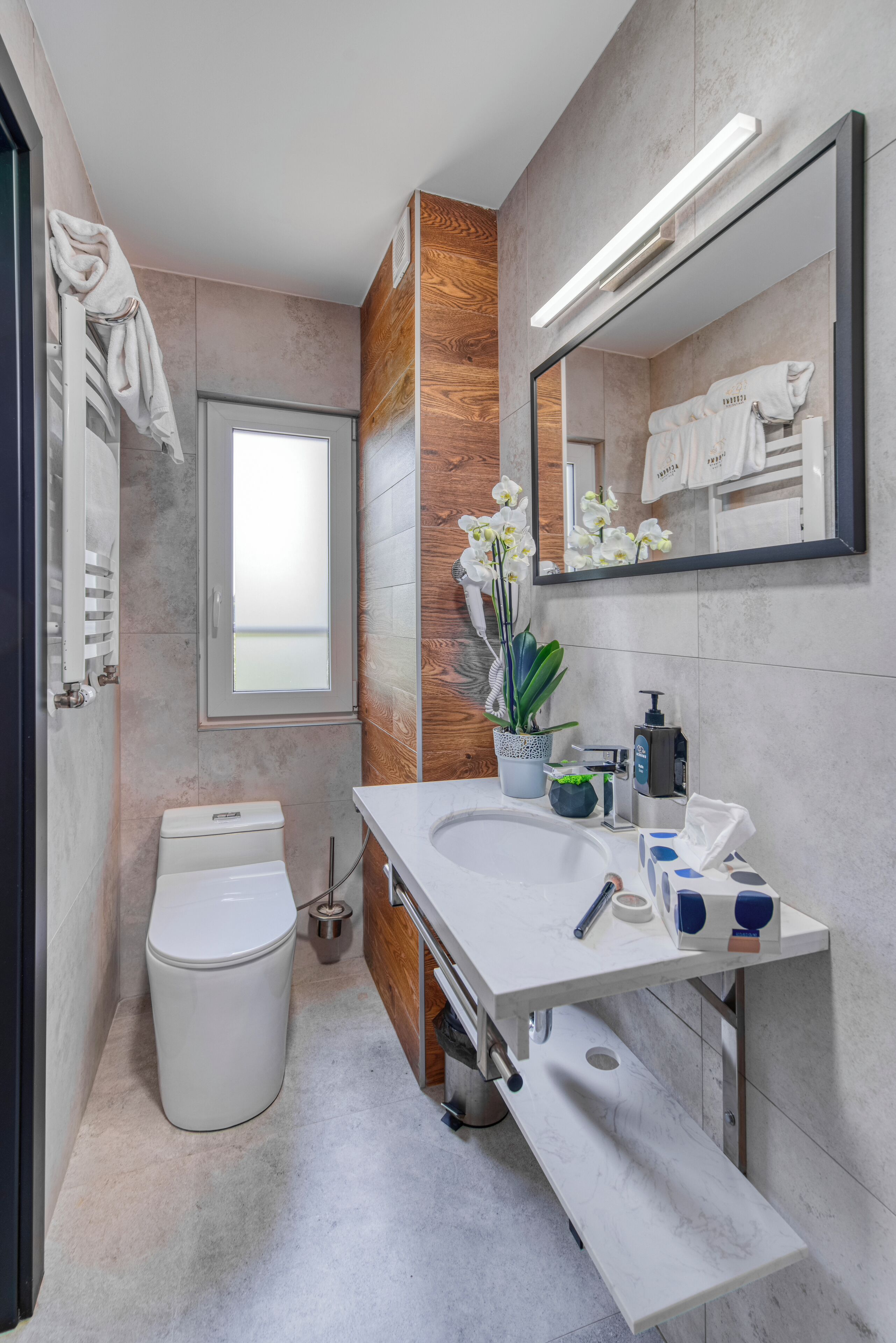 A modern bathroom with a toilet, sink, mirror, and a window.