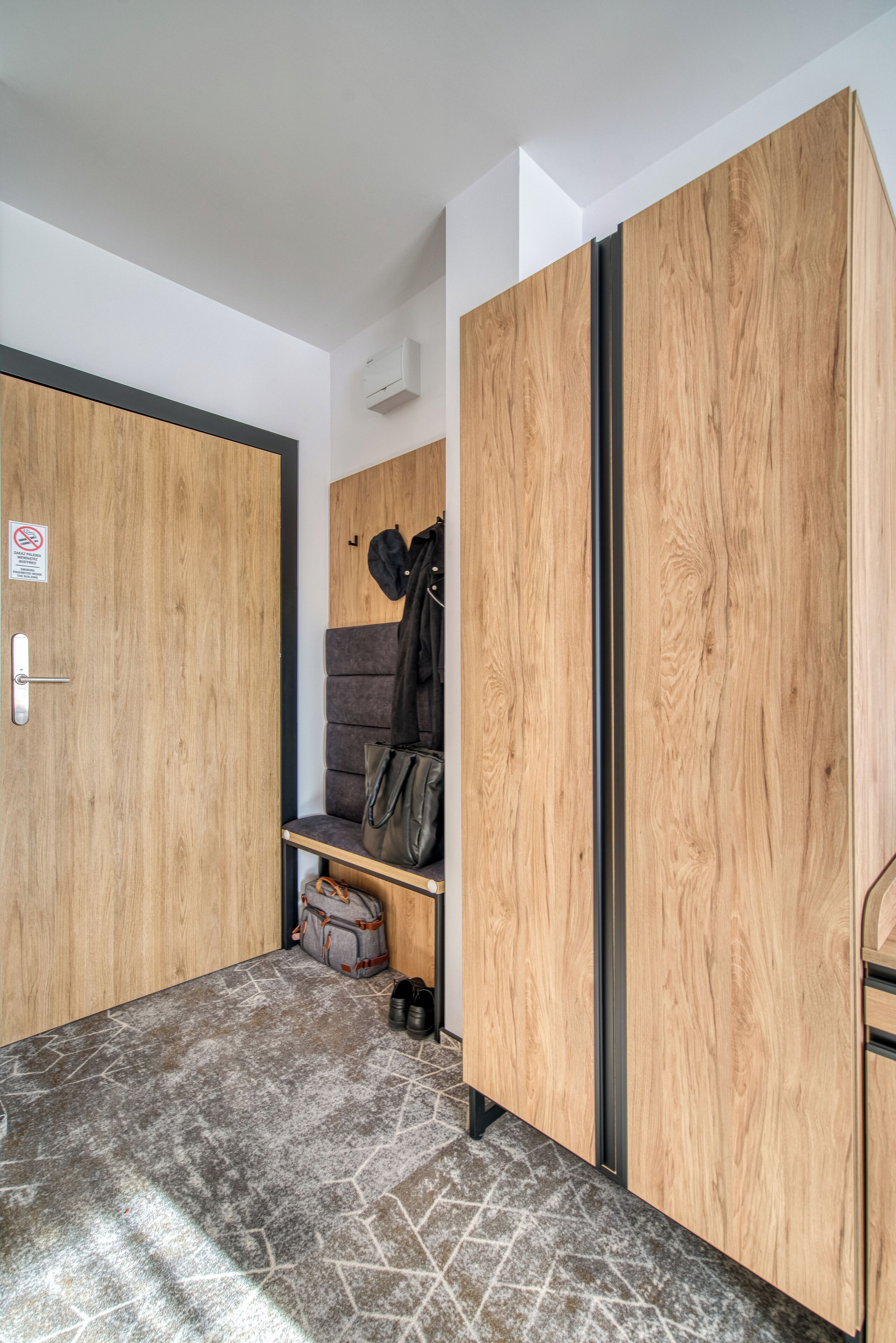 A modern room with wooden wardrobes, a grey sofa, and a coat rack.